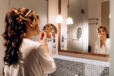 bride in a veil with makeup paints her lips in the bathroom