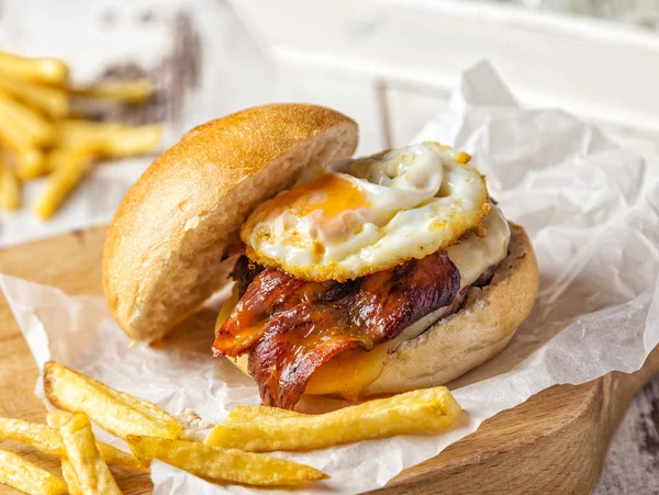 Pastırma ve yumurta burger ev yapımı patates kızartması ile bir kesme tahtası üzerinde servis.