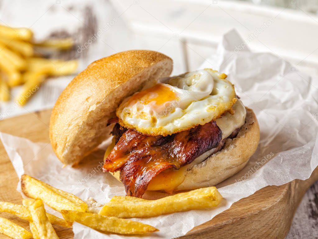 Bacon and egg burger served on a cutting board with homemade fries.