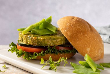 Yeşil fasulye ve nohuttan yapılmış vejetaryen hamburger, domates, salatalık ve marulla servis edilir..