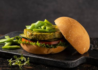 Yeşil fasulye ve nohuttan yapılmış vejetaryen hamburger, domates, salatalık ve marulla servis edilir..