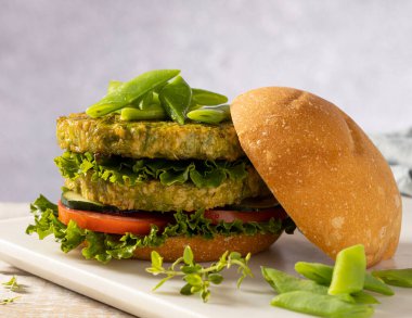 Yeşil fasulye ve nohuttan yapılmış vejetaryen hamburger, domates, salatalık ve marulla servis edilir..