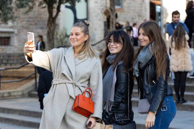 BARCELONA, SPAIN - 23 Kasım 2019: Üç genç kadın bir alışveriş haftasonunun bir parçası olarak Barselona katedralinin önünde selfie çekiyor.