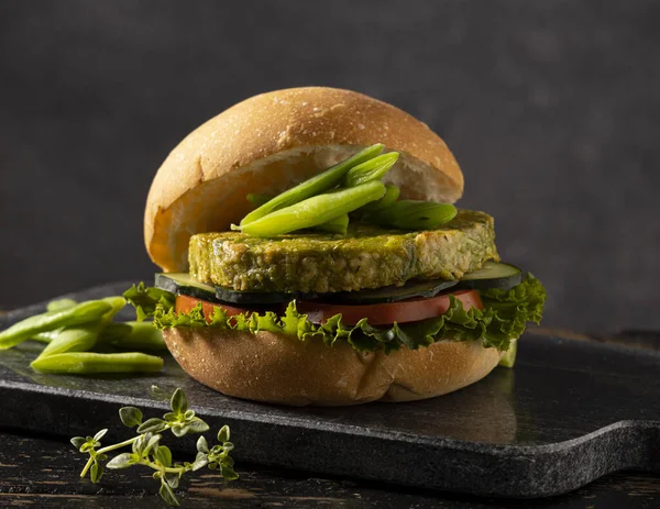 Yeşil fasulye ve nohuttan yapılmış vejetaryen hamburger, domates, salatalık ve marulla servis edilir..