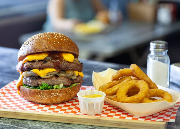 A double cheeseburger with dripping melted cheese served with onion rings at a fast food restaurant.