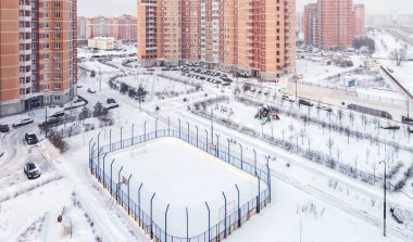 Çocuk parkı hokey stadyumunun panoramik manzarası ve yüksek katlı bina cephesi. Karışık kullanımlı kentsel yerleşim bölgesi gelişimi soğuk kar beyazı kış günü.