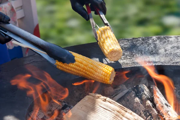 Two roasted sweet corns holding barbecue tongs open fire grill with firewood happy sunny day — Stock Photo, Image