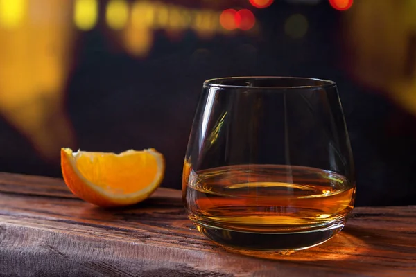 Szklanka whisky z pomarańczowym plasterkiem drewniany stół bar żółty czerwony światło bokeh tło — Zdjęcie stockowe