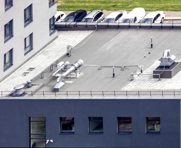 Top view gray flat roof with air conditioners and hydro insulation membranes modern dark blue apartment building with car sunny summer day background.