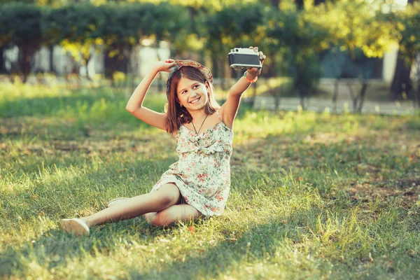 少女は 公園の草の上に座って写真をカメラで再生されます Selfie の周りの世界を撮影して — ストック写真