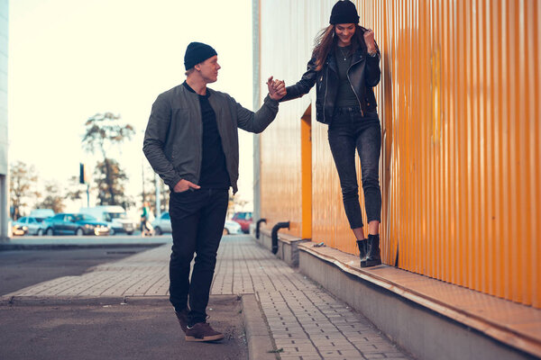 Young couple in love walks by the sity. Spring, autumn. The guy is wearing a jacket and hat. Girl in a hat and leather jacket with a scarf