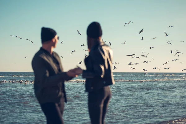Молодая пара влюбленных гуляет по морю. Весна, осень. На парне куртка и шляпа. Девушка в шляпе и кожаной куртке с шарфом — стоковое фото