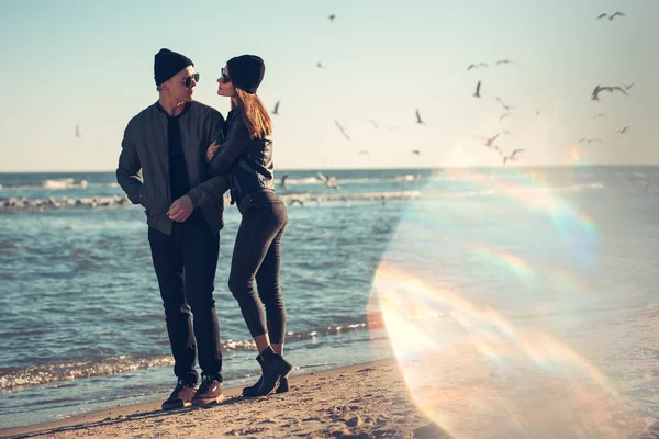 Young couple in love walks by the sea. Spring, autumn. The guy is wearing a jacket and hat. Girl in a hat and leather jacket with a scarf