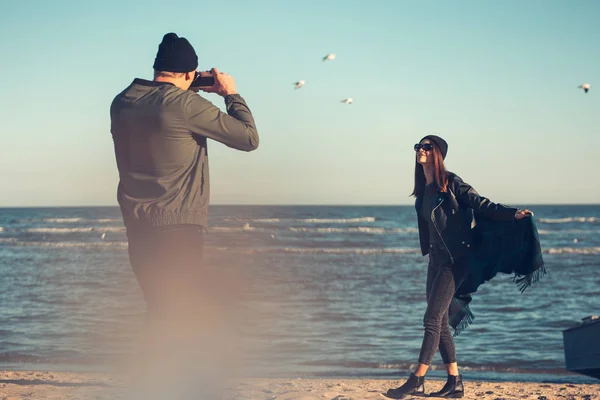 Young couple in love walks by the sea. Spring, autumn. The guy is wearing a jacket and hat. Girl in a hat and leather jacket with a scarf