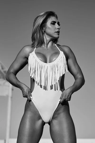 Erstaunliche sexy Frau im weißen Badeanzug mit perfektem Sportkörper posiert am Strand. Konzept des Sports Frauenkörper in Badebekleidung — Stockfoto