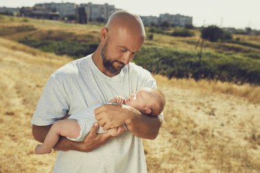 genç baba doğada yürürken yeni doğmuş bir bebek tutar. Mutlu baba şort ve tişört giyiyor. Uluslararası Babalar Günü