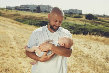genç baba doğada yürürken yeni doğmuş bir bebek tutar. Mutlu baba şort ve tişört giyiyor. Uluslararası Babalar Günü