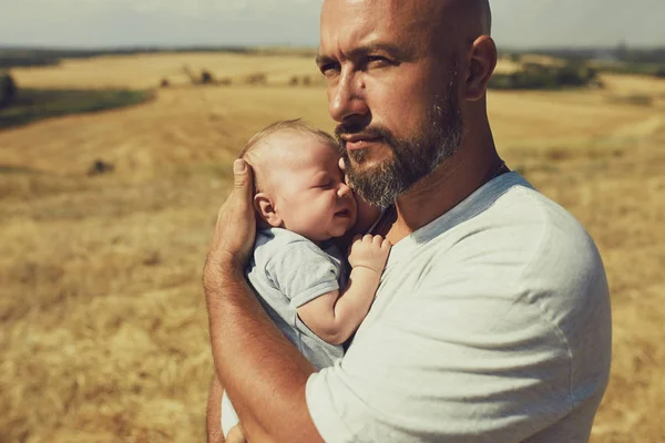 Der junge Vater hält beim Spazierengehen in der Natur ein Neugeborenes in der Hand. Der glückliche Vater trägt kurze Hosen und ein T-Shirt. Internationaler Vatertag — Stockfoto