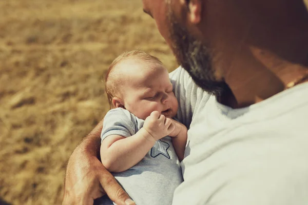 Der junge Vater hält beim Spazierengehen in der Natur ein Neugeborenes in der Hand. Der glückliche Vater trägt kurze Hosen und ein T-Shirt. Internationaler Vatertag — Stockfoto