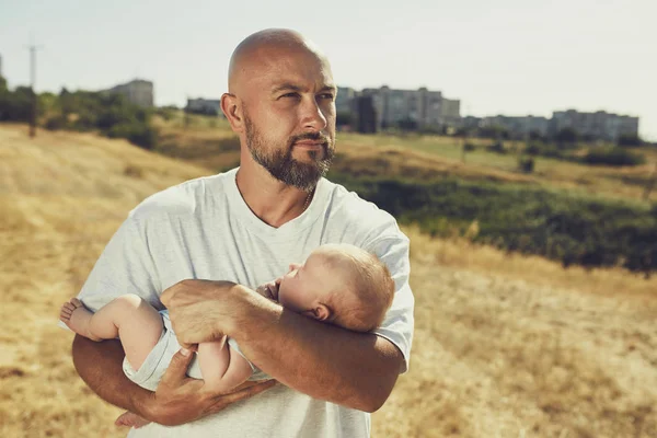 年轻的爸爸抱着一个新生婴儿，而走在大自然。快乐的父亲穿着短裤和T恤。国际父亲节 — 图库照片