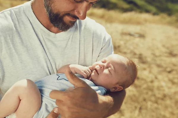 Der junge Vater hält beim Spazierengehen in der Natur ein Neugeborenes in der Hand. Der glückliche Vater trägt kurze Hosen und ein T-Shirt. Internationaler Vatertag — Stockfoto