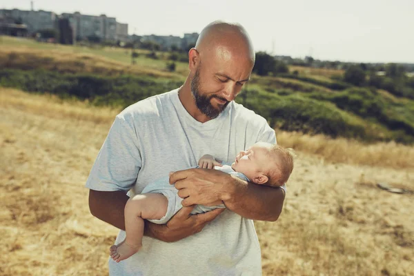 young dad holds a newborn baby while walking in nature. happy father is wearing shorts and a t-shirt. International Father's Day