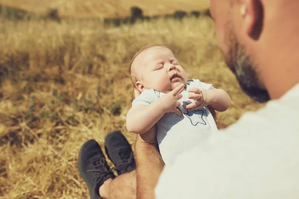 Der junge Vater hält beim Spazierengehen in der Natur ein Neugeborenes in der Hand. Der glückliche Vater trägt kurze Hosen und ein T-Shirt. Internationaler Vatertag — Stockfoto