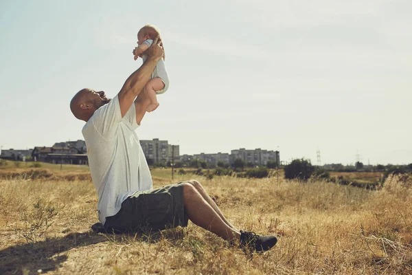 Молодий тато тримає новонародженого малюка на його витягнутих руках. щасливий батько носить шорти та футболку. Міжнародний День батька — стокове фото