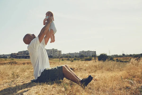 年轻的爸爸把一个刚出生的婴儿抱在伸出的胳膊上。快乐的父亲穿着短裤和T恤。国际父亲节 — 图库照片