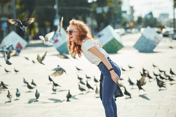 Mooie roodharige meisje met plezier op straat. De meiden hebben een mooi figuur, een wit T-shirt en een jeans met zonnebril — Stockfoto