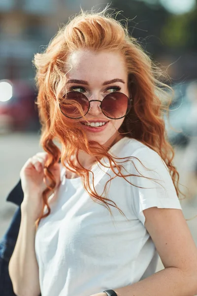 Hermosa chica pelirroja divirtiéndose en la calle. Las chicas tienen una hermosa figura, una camiseta blanca y jeans con gafas de sol —  Fotos de Stock