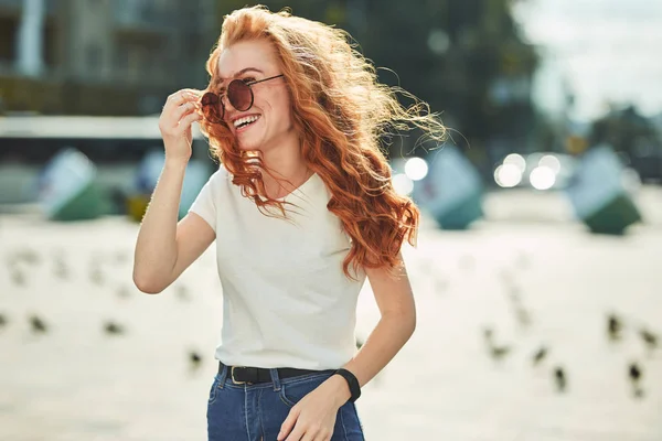 Schöne rothaarige Mädchen, die Spaß auf der Straße haben. die Mädchen haben eine schöne Figur, ein weißes T-Shirt und Jeans mit Sonnenbrille — Stockfoto