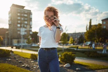 Çekici kızıl saçlı, şirin yüzlü bir kızın portreleri. Şehir merkezinde kameraya poz veren bir kız. Harika bir ruh hali ve güzel bir gülümsemesi var.