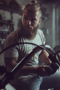 Yakışıklı sakallı adam bir motosiklet koltuğunda oturur ve uzağa bakar