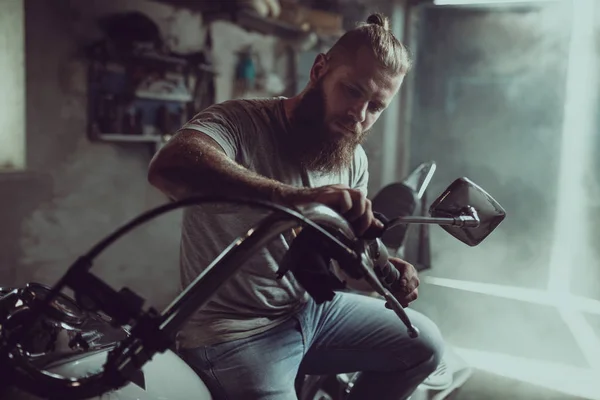 Yakışıklı sakallı adam bir motosiklet koltuğunda oturur ve direksiyon tamir — Stok fotoğraf