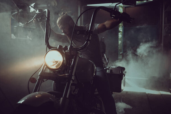 Handsome brutal man with a beard sitting on a motorcycle in his garage