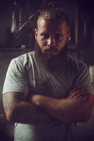 Bonito homem brutal com uma barba em pé em sua garagem contra o fundo de ferramentas de reparo — Fotografia de Stock