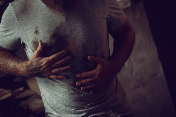 Bonito homem brutal com uma barba fica em sua garagem contra o fundo de ferramentas de reparo e limpa as mãos em sua camisa — Fotografia de Stock