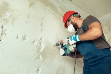 Beton duvarda delik açan inşaatçı koruyucu kostüm ve kask giymiş.