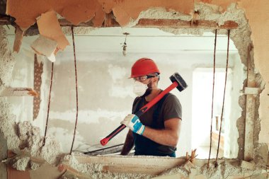 Elinde çekiçle inşaatçı beton duvarı yıkar inşaatçı koruyucu bir kostüm ve kask giyer.