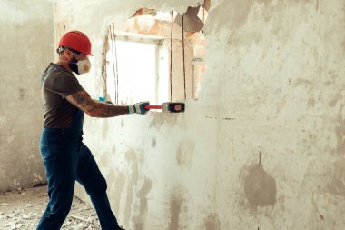 Elinde çekiçle inşaatçı beton duvarı yıkar inşaatçı koruyucu bir kostüm ve kask giyer.
