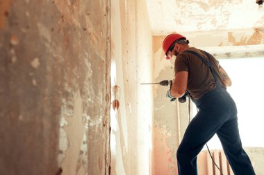 Beton duvarda delik açan inşaatçı koruyucu kostüm ve kask giymiş.