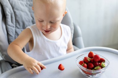Gülümseyen küçük çocuk çilek yiyor.