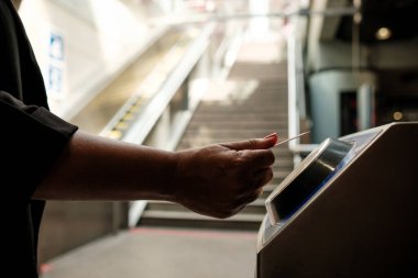 İş kadını metro istasyonunun girişine elektronik bilet yerleştiriyor. Arka planda yürüyen merdiven ve merdivenler var. Toplu taşımaya erişim sağlıyor.
