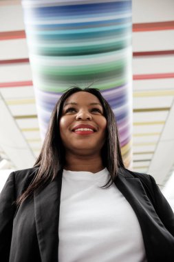 Gülümseyen bir iş kadınının, renkli bir tavan tasarımının yarattığı canlı bir atmosferle çevrili modern bir binada güvenle yürürken alçak açılı bir görüntüsünü yakalamak.