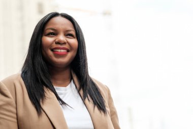 Kendine güvenen iş kadını bej takım elbise giyiyor ve beyaz gömlek yukarı bakarken gülümsüyor, pozitifliğini, başarısını ve hırsını parlak bir ortamda ifade ediyor.