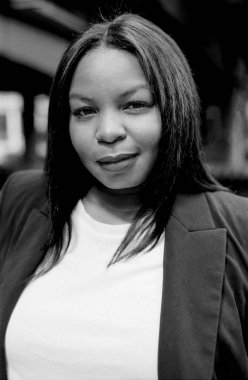 Yüzü biraz bulanık bir şehir ortamında güven ve profesyonellik saçan gülümseyen bir iş kadınının tek renkli, orta formatlı film portresi.