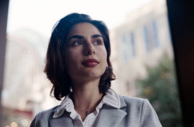 Young businesswoman with a thoughtful expression is looking up while standing near a window, showcasing ambition and future vision in an urban setting with a vintage analog film look