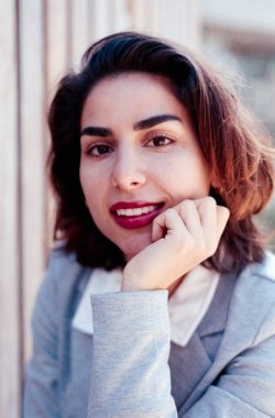 Woman with red lipstick smiling, hand on chin in a warm, confident 35mm film portrait; vintage grain and soft focus give a candid, stylish, nostalgic headshot vibe