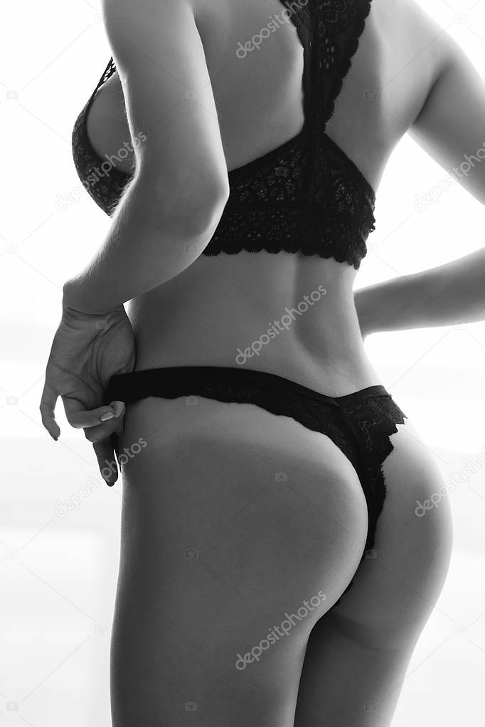 Black and white crop side view of faceless naked female standing and keeping hands on thong